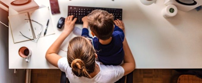 A woman works on a computer at a desk with a child sat in her lap