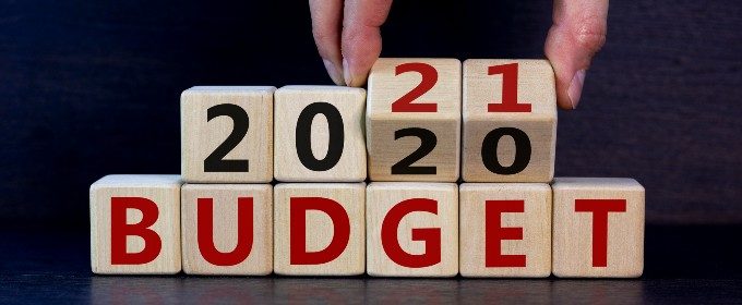 A man turns wooden number blocks to reveal the phrase '2021 BUDGET' against a black background